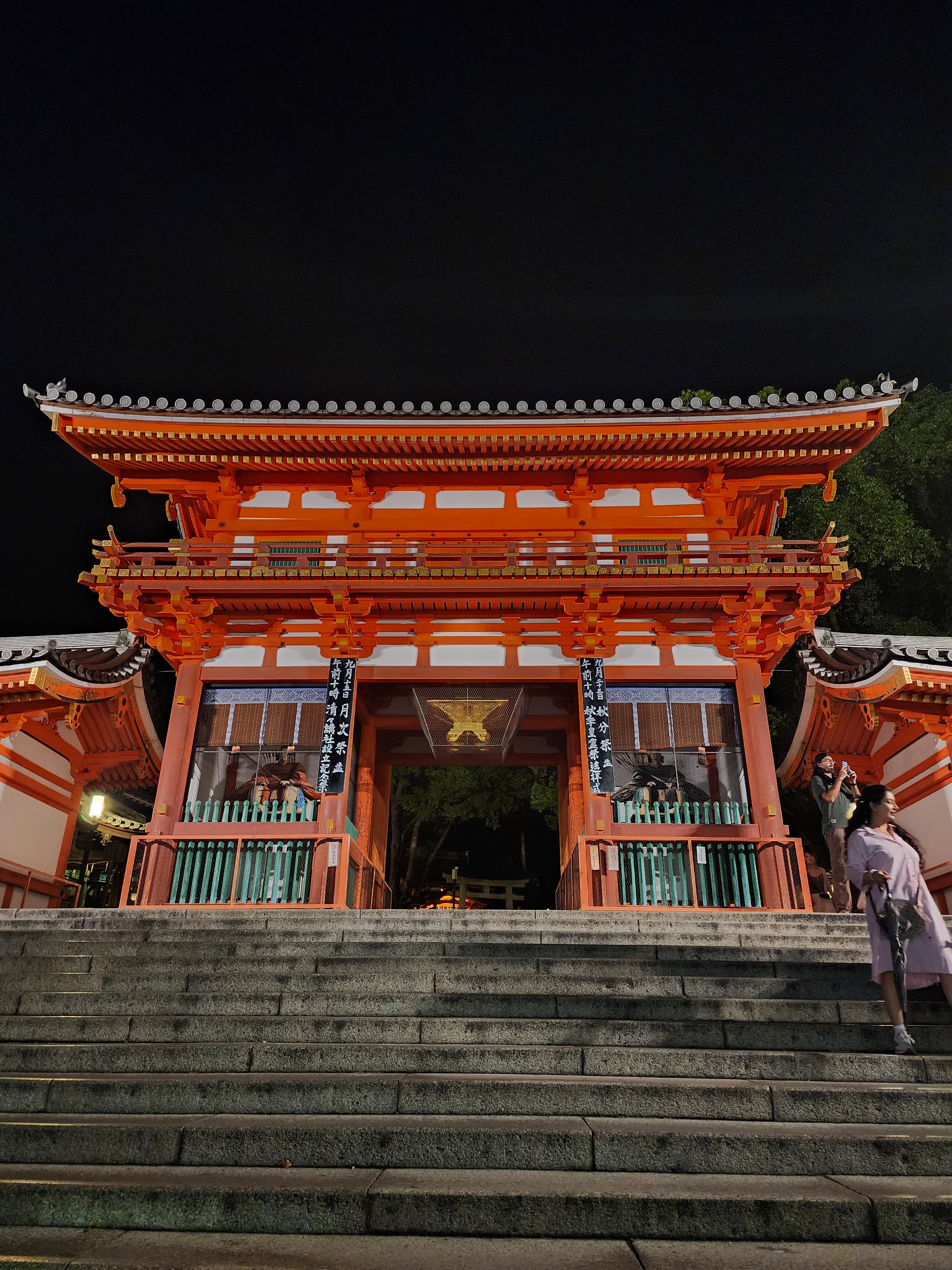 Puerta roja de santuario japonés iluminada de noche sobre una gran escalinata de piedra.