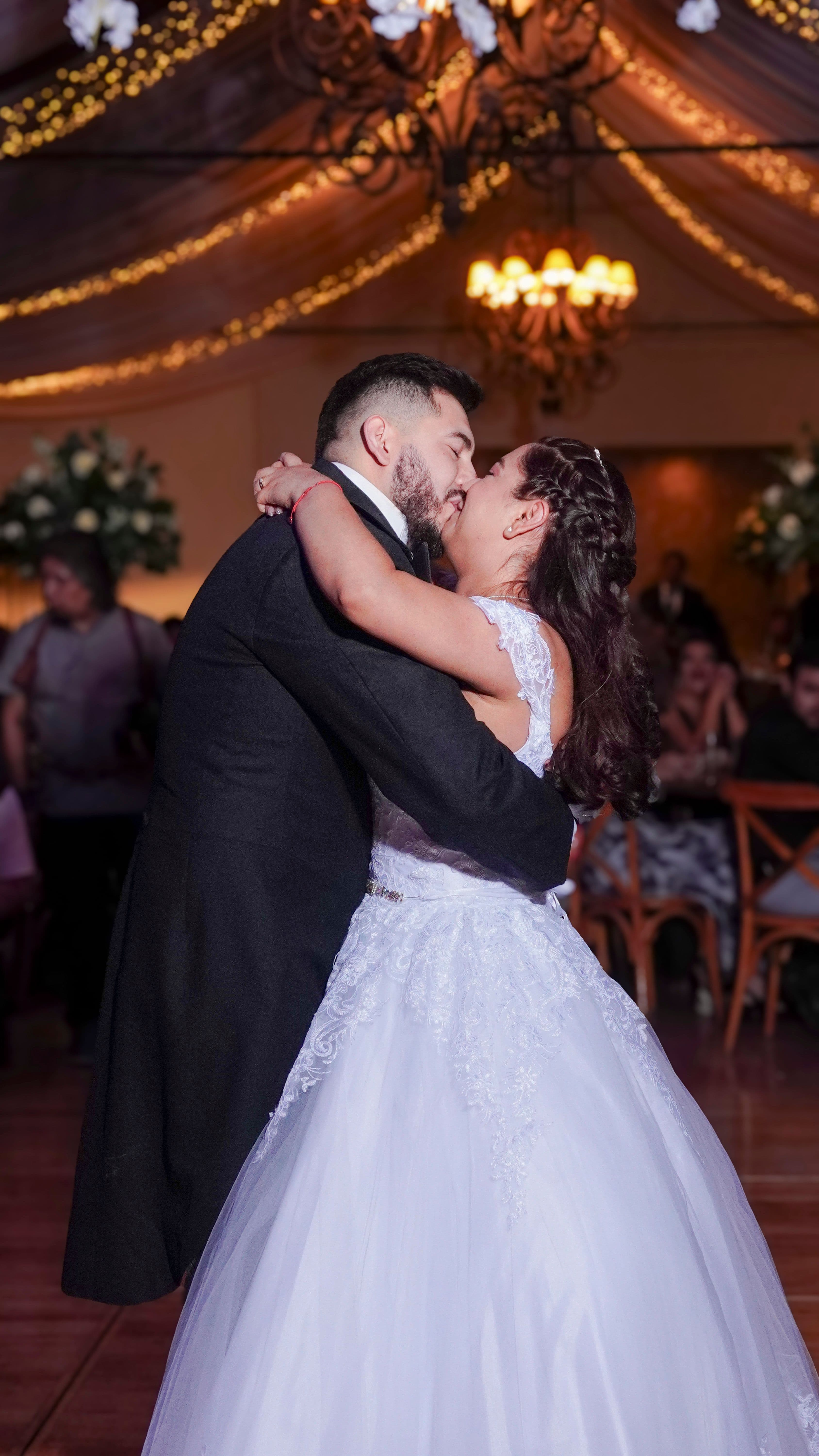 Novia y novio se besan románticamente mientras bailan en su recepción de boda iluminada.