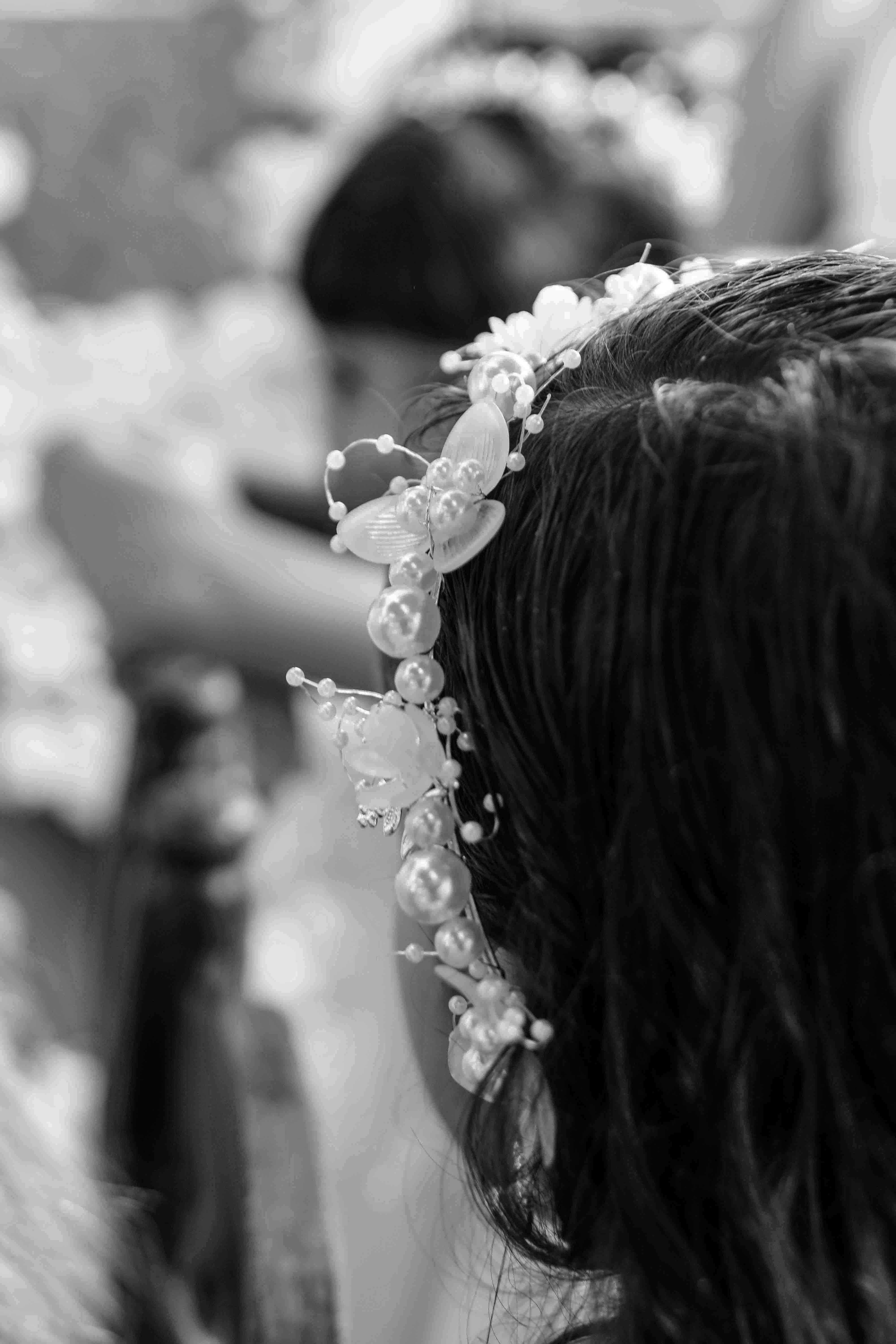 Detalle de una diadema con perlas y flores sobre cabello oscuro en blanco y negro.