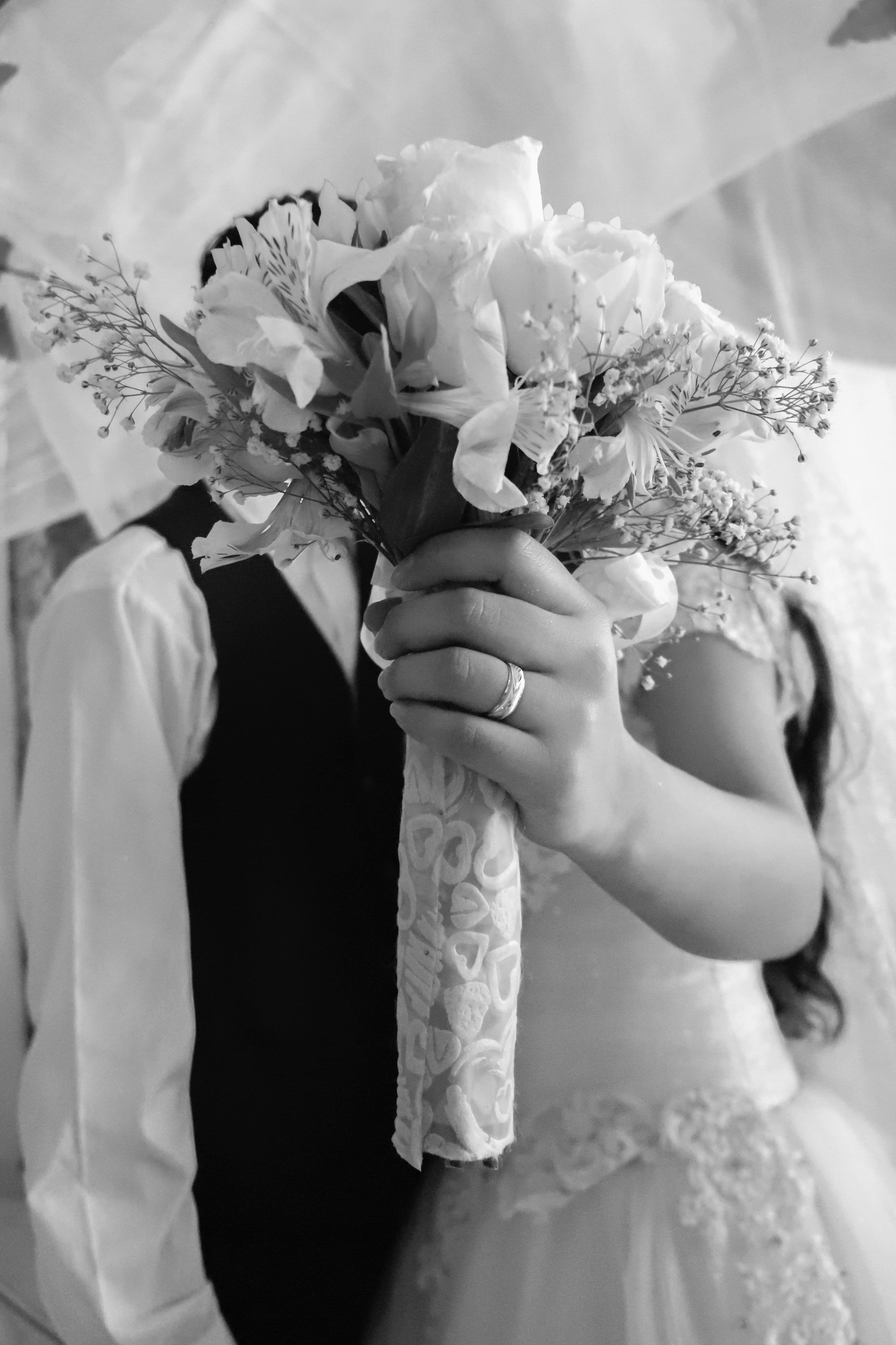 Novia con anillo de bodas sostiene un ramo de flores blancas ocultando los rostros.