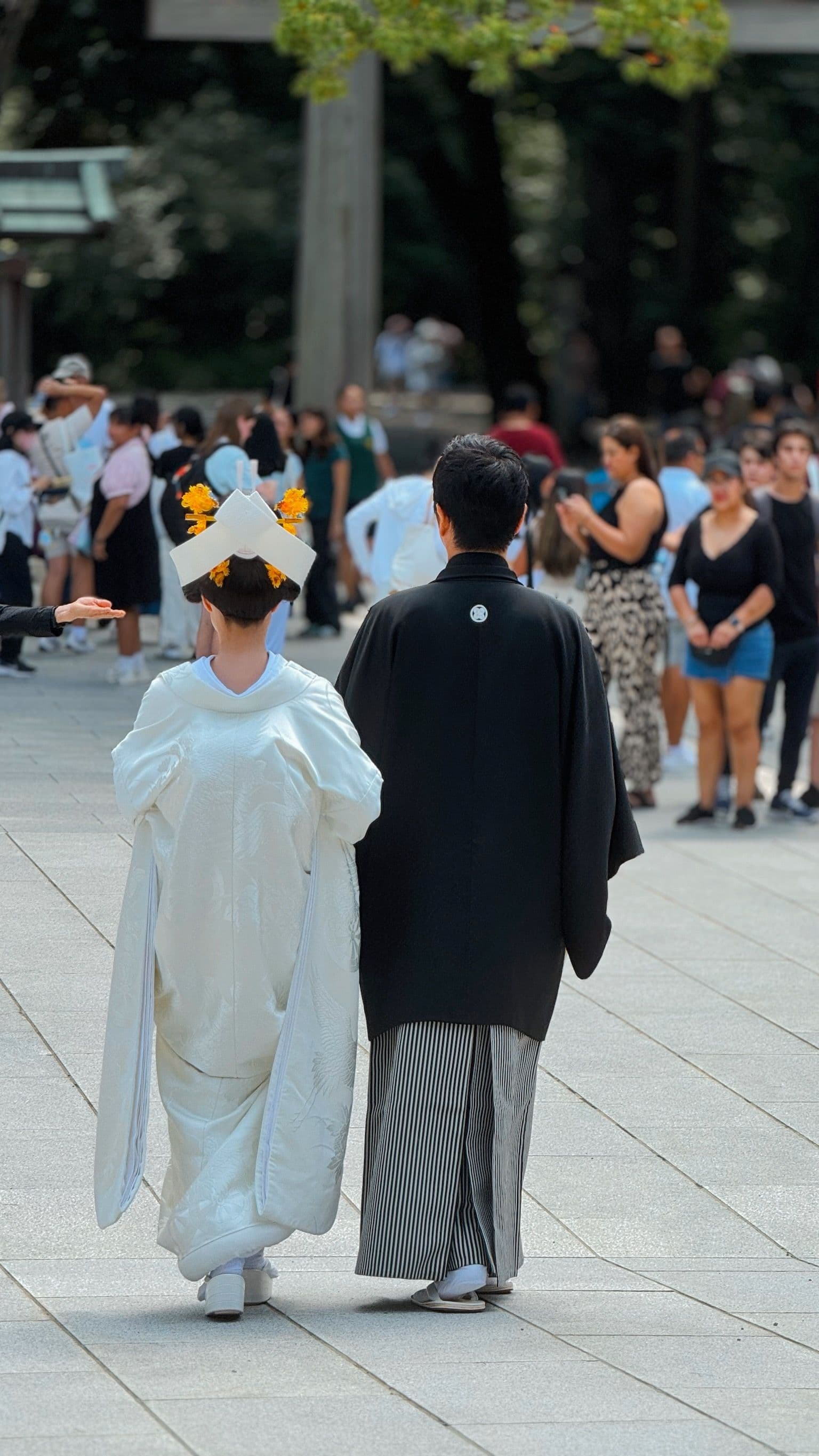 Novios con trajes tradicionales japoneses caminan de espaldas por un sendero de piedra concurrido.