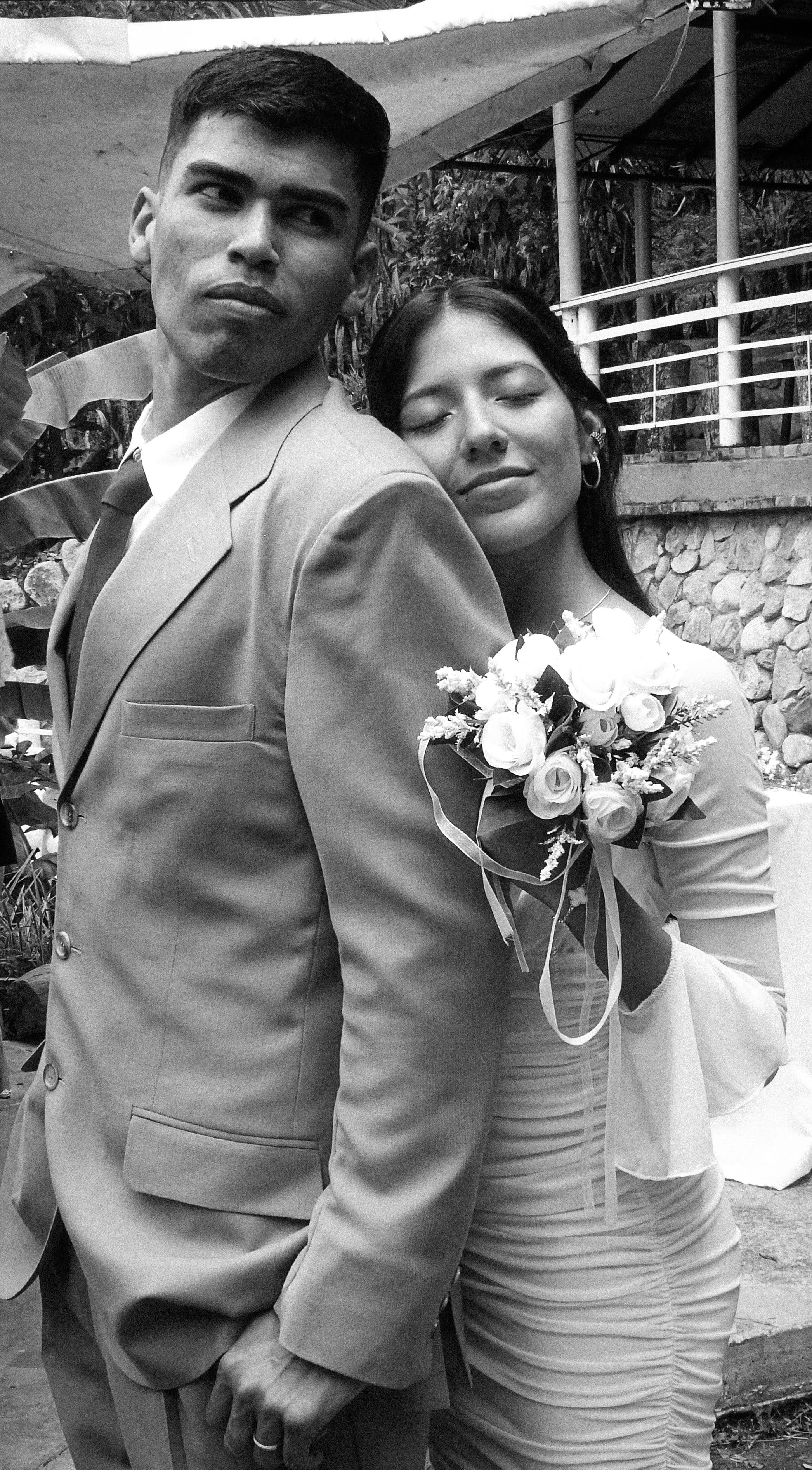 Novia con ramo de rosas apoyada en el hombro del novio, blanco y negro.