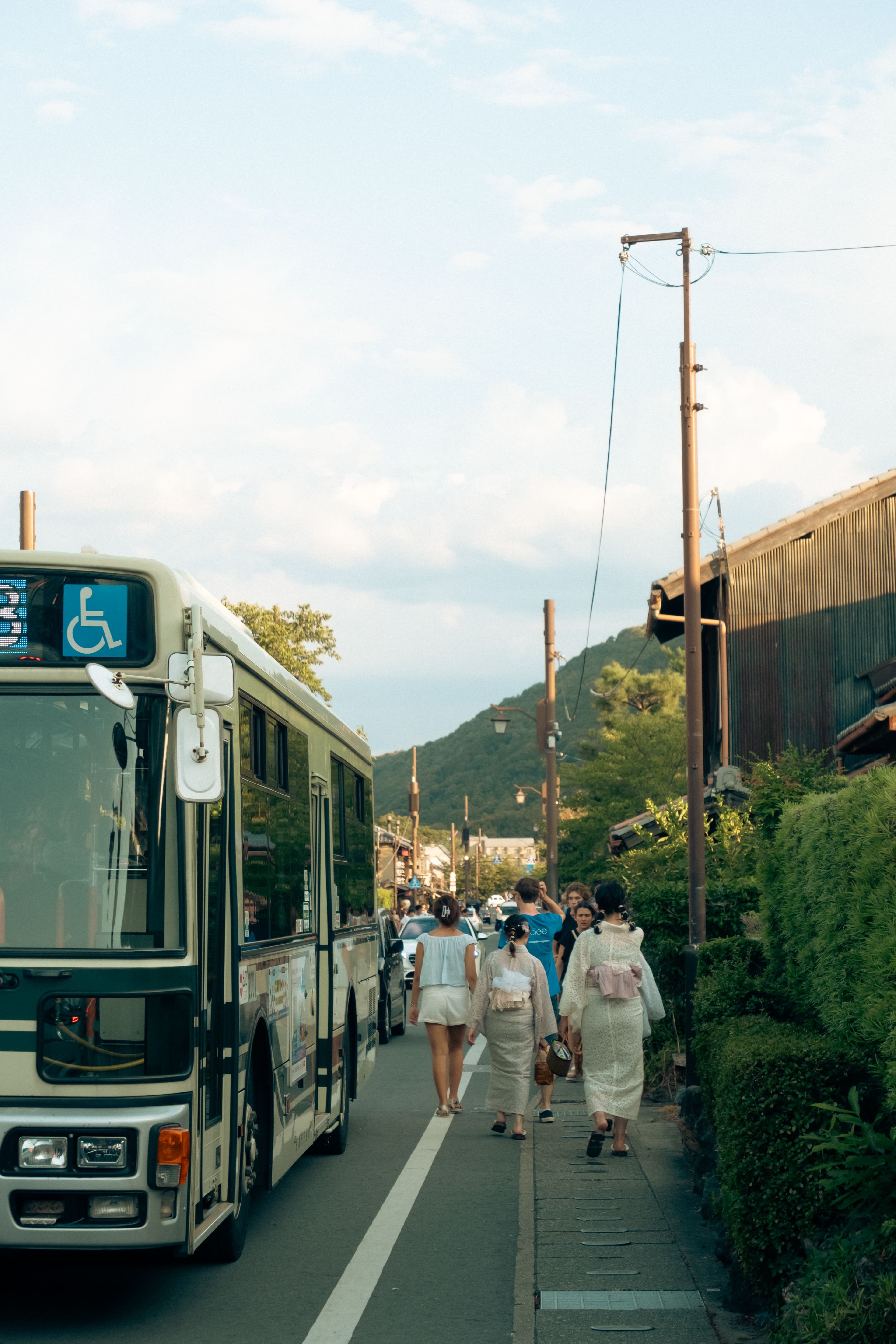 Autobús en calle japonesa con mujeres en kimono caminando hacia una montaña al fondo.